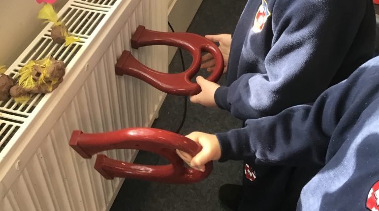 Two children with big plastic horse shoes stood next to a radiator.