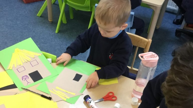 Child making a house by cutting out pieces of paper and sticking them onto another piece of paper