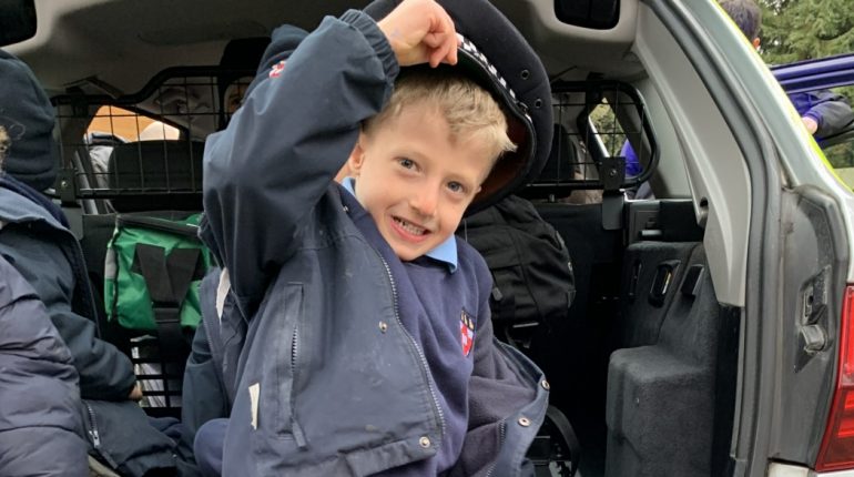 Child wearing a police hat at the boot of the car